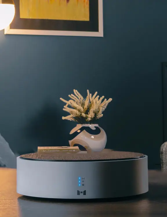MHub من MTronic موضوع على طاولة بنية مع ثلاثة أضواء زرقاء عمودية مضاءة وشعار MTronic في الأسفل وسط؛ مزهرية، جدران زرقاء وملصق أصفر مع خطوط بيضاء وسوداء في الخلفية.